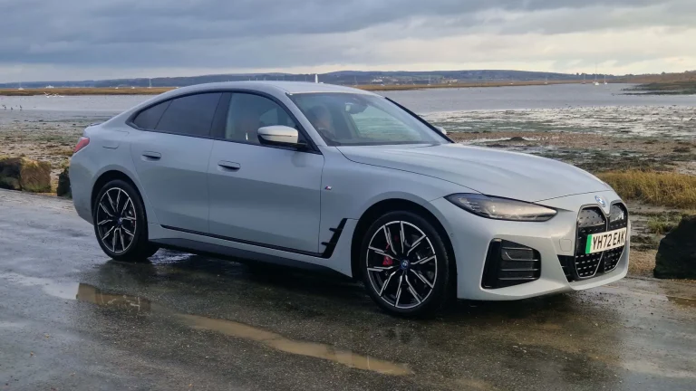 A BMW I4 is stanidng on a wet road near a shore