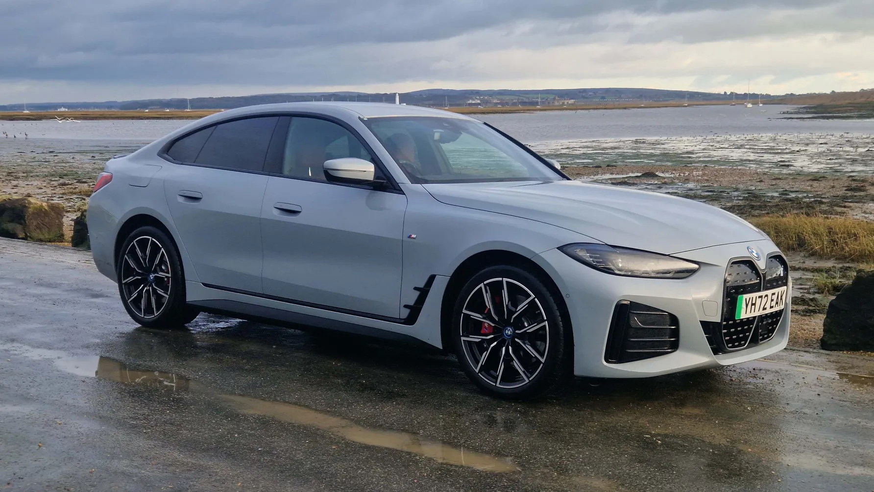 A BMW I4 is stanidng on a wet road near a shore