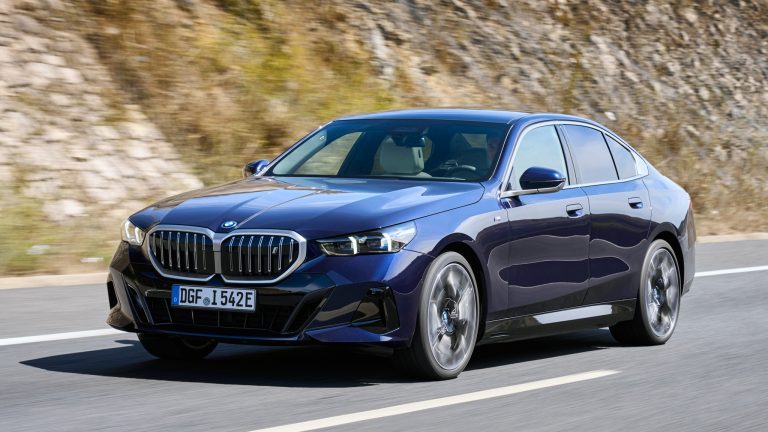 BMW i5 speeds along a winding road, showcasing its modern design and refined electric performance