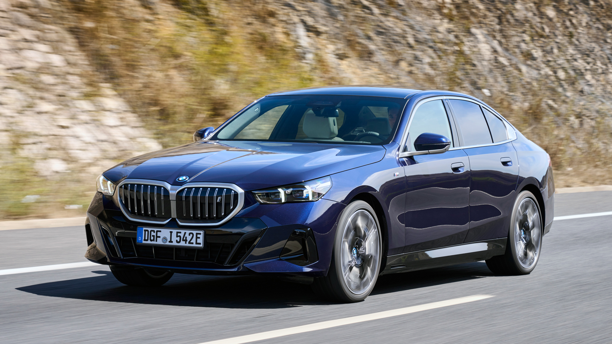 BMW i5 speeds along a winding road, showcasing its modern design and refined electric performance