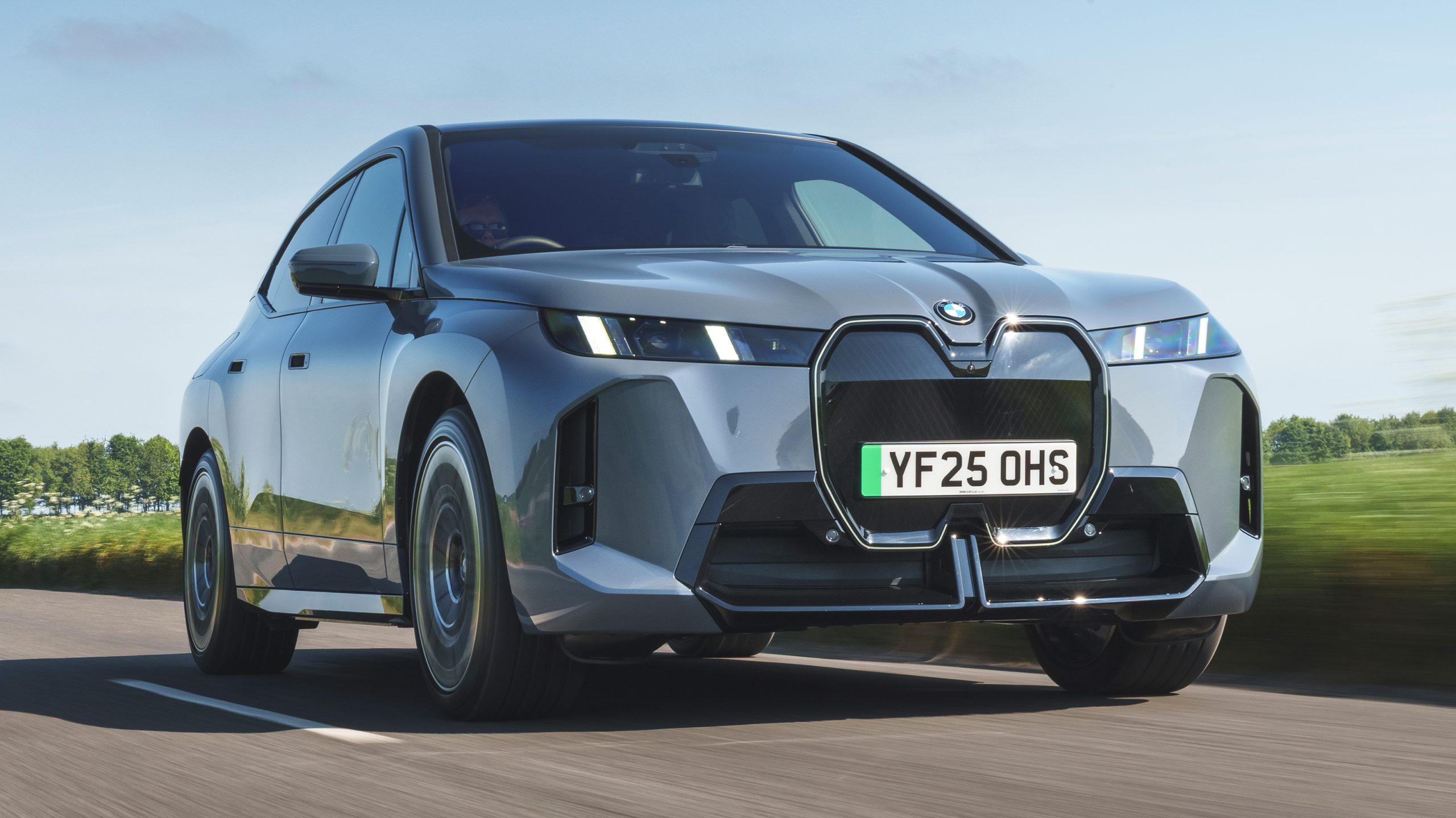 BMW iX electric SUV cruises along a country road, showcasing its bold front design