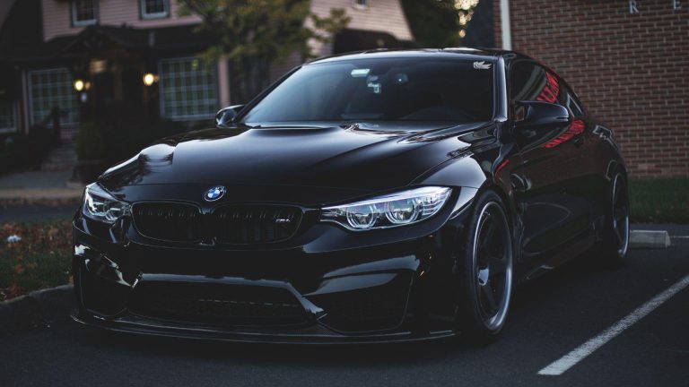 Black BMW M4 parked outdoors at dusk, highlighting its aggressive styling and illuminated headlights