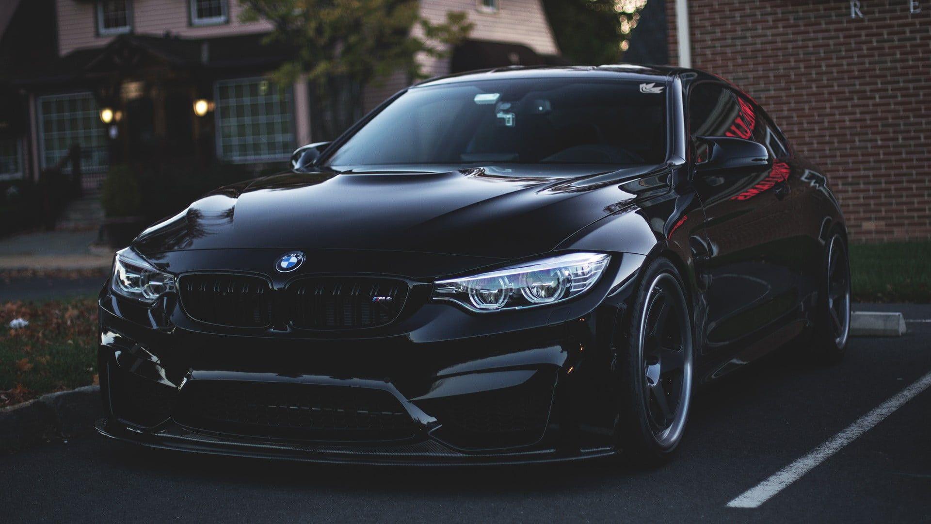 Black BMW M4 parked outdoors at dusk, highlighting its aggressive styling and illuminated headlights