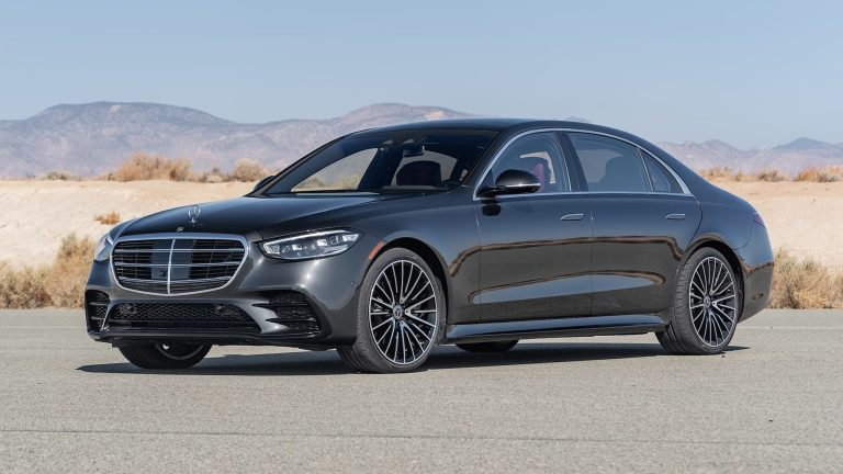 Black Mercedes-Benz S-Class sedan parked on a desert road with mountains in the background