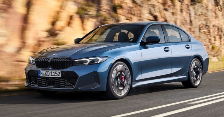 Blue BMW 3 Series sedan driving along a sunlit road beside rocky cliffs