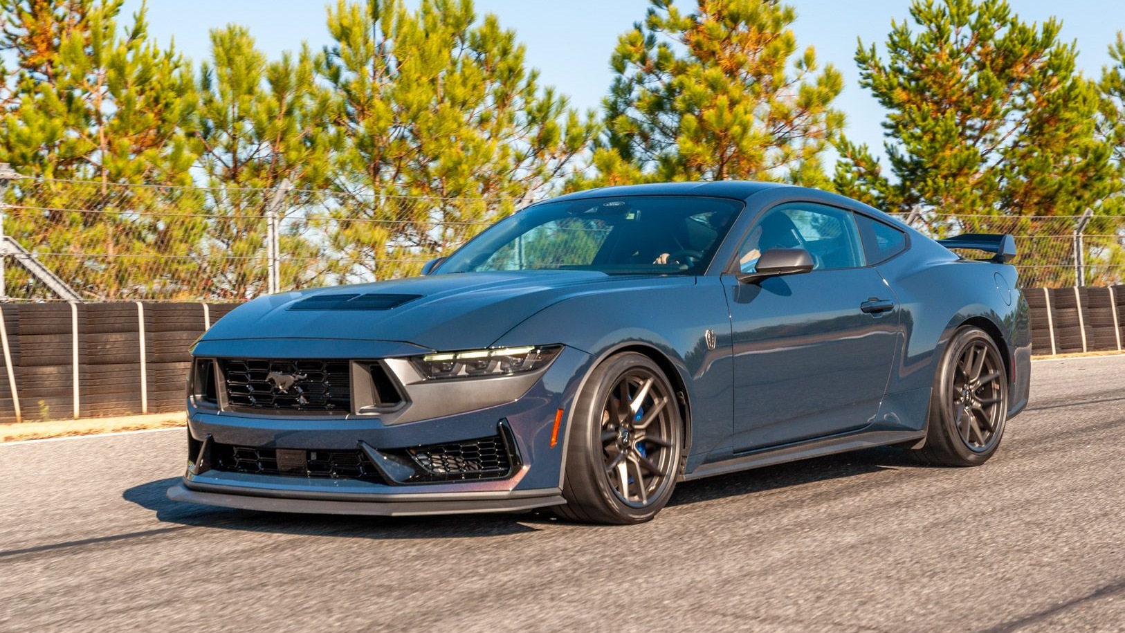 Blue Ford Mustang Dark Horse driving on a racetrack, showcasing its aggressive performance styling