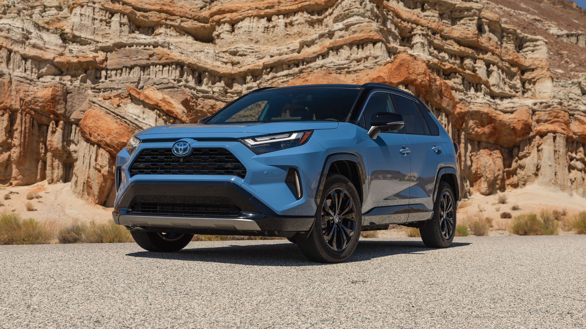 Blue Toyota RAV4 parked against dramatic desert rock formations, highlighting its rugged crossover styling