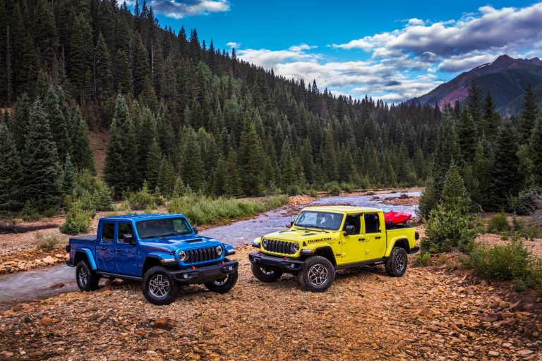 Blue and yellow Jeep Gladiator pickups parked beside a rocky river in a forested mountain setting