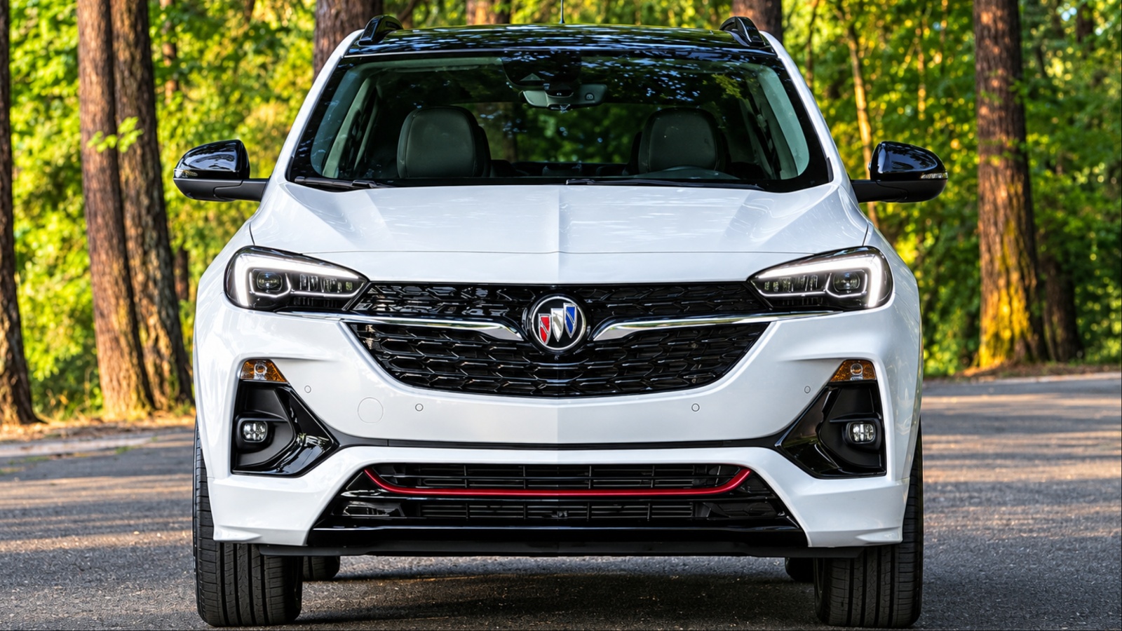 White Buick Encore GX SUV faces camera on wooded road