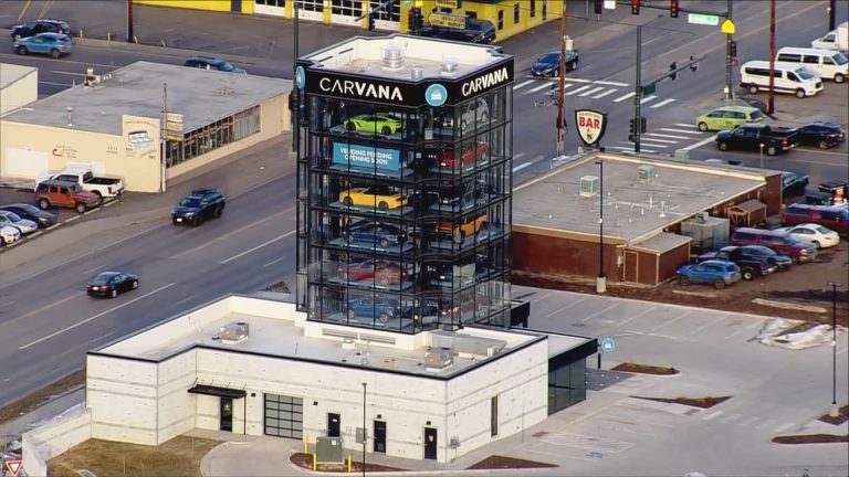 Carvana’s glass vehicle vending tower displays multiple cars above a modern dealership building