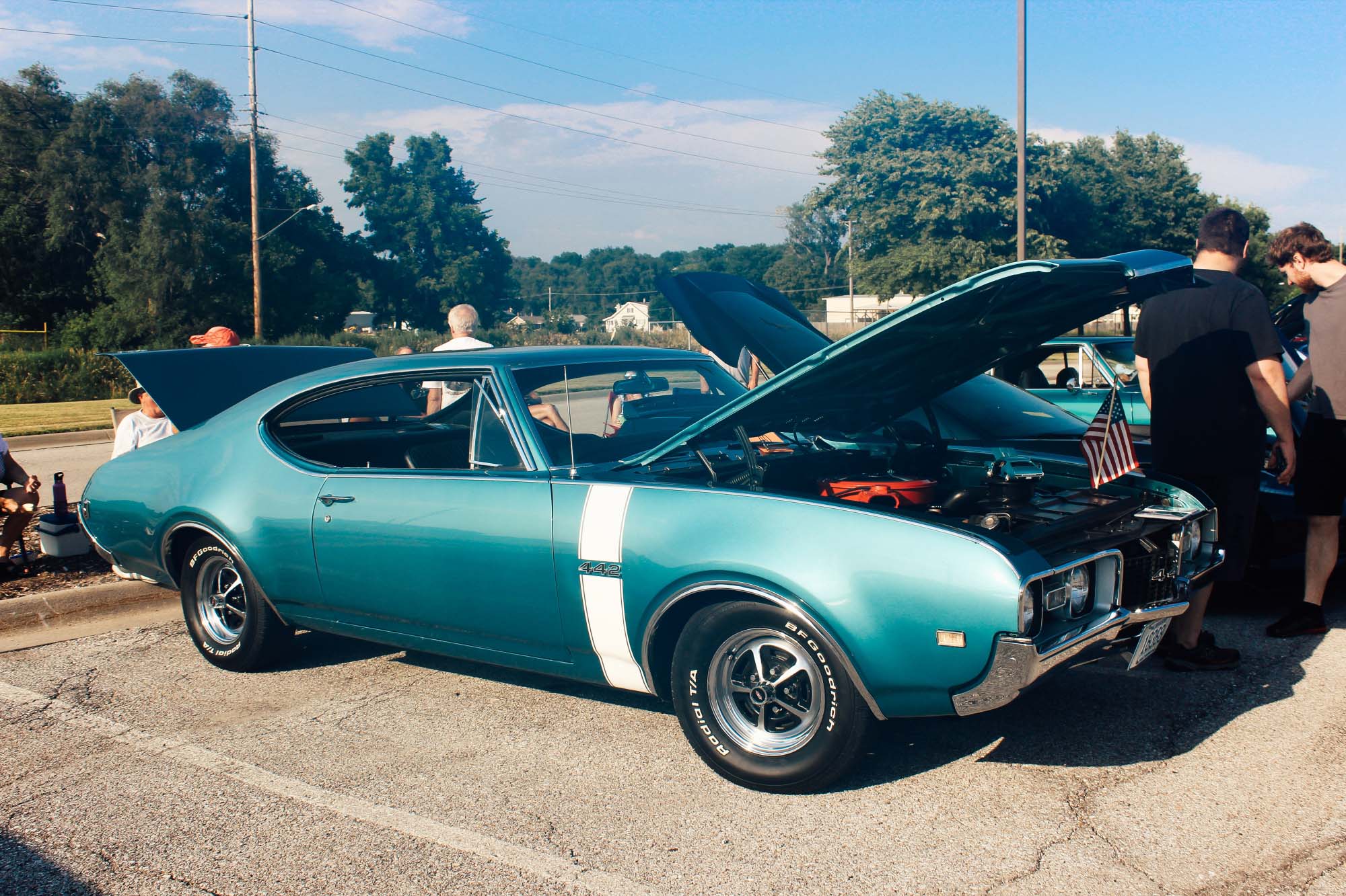 Classic turquoise Oldsmobile 442 muscle car displayed at an outdoor car show with its hood open