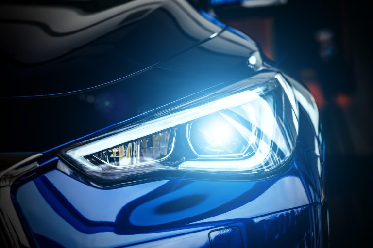 Close-up of a bright car headlight illuminating the front bodywork in darkness