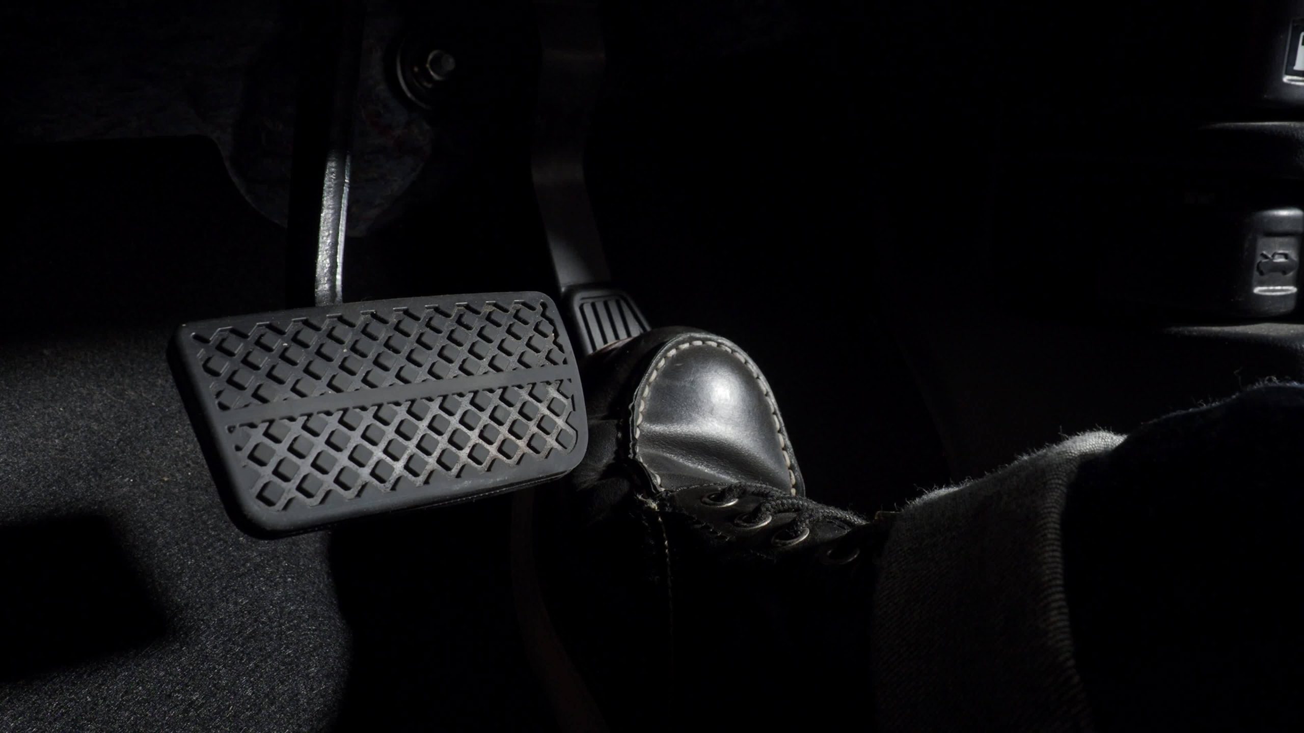 Close-up of a driver’s foot pressing the brake pedal inside a dark car interior