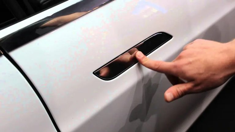 Close-up of a hand pressing a flush-mounted hidden door handle on a modern car