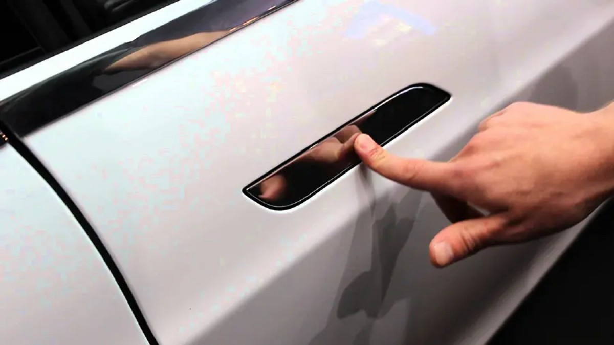 Close-up of a hand pressing a flush-mounted hidden door handle on a modern car