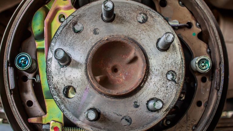 Close-up of a worn drum brake assembly showing the wheel hub, studs, springs, and brake components