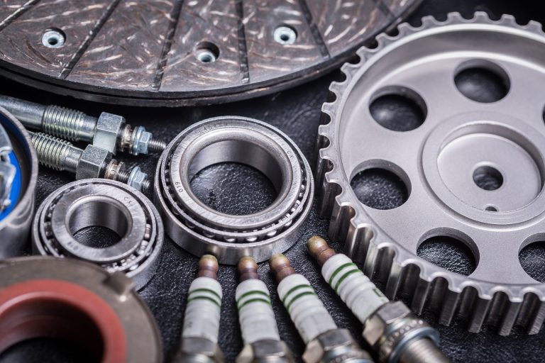 Close-up of automotive components featuring metal bearings, timing gears, spark plugs, and threaded fasteners
