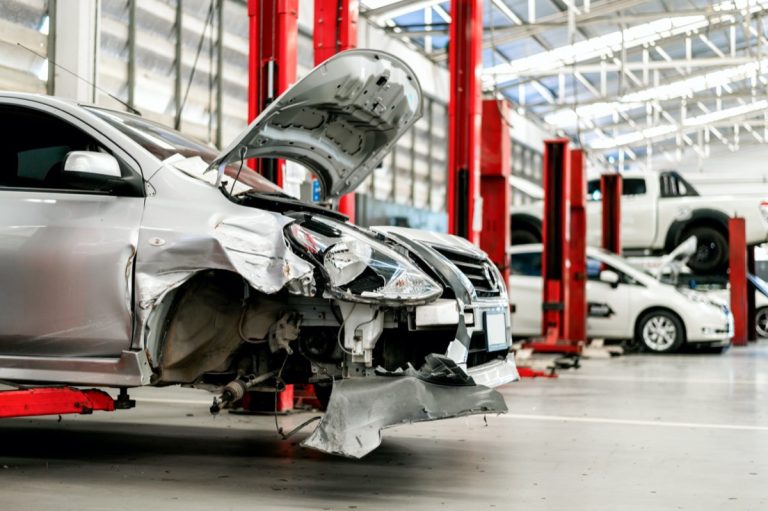 Damaged car with severe front-end collision damage undergoing inspection and repairs at an auto body shop