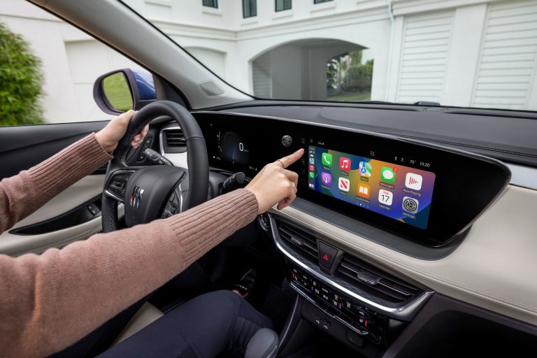 Driver interacts with the Buick Encore GX touchscreen, showcasing Apple CarPlay and dashboard technology