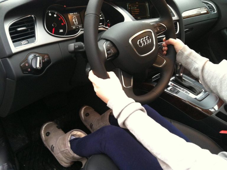 Driver seated inside an Audi, holding the steering wheel while operating the center console controls