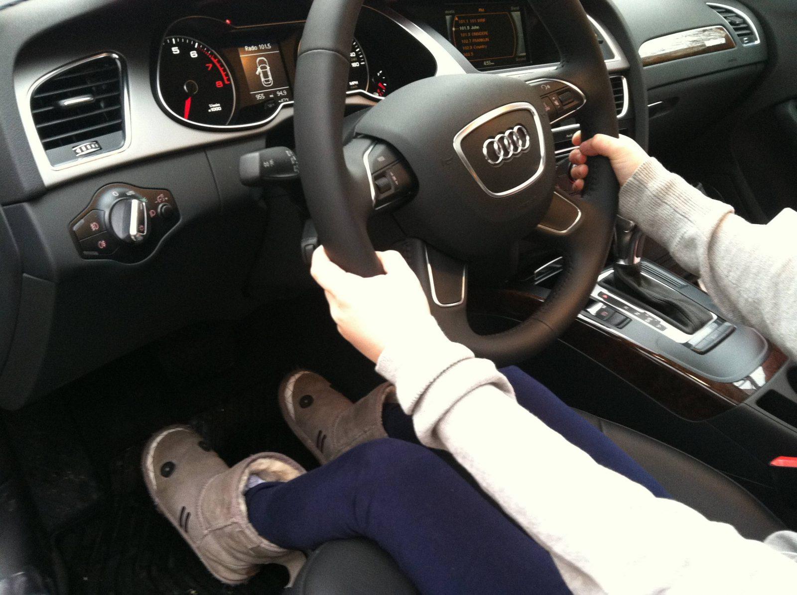 Driver seated inside an Audi, holding the steering wheel while operating the center console controls