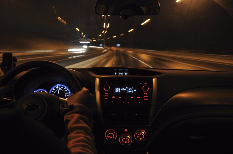 Driver’s-eye view of a car traveling through a tunnel at night, with illuminated dashboard instruments