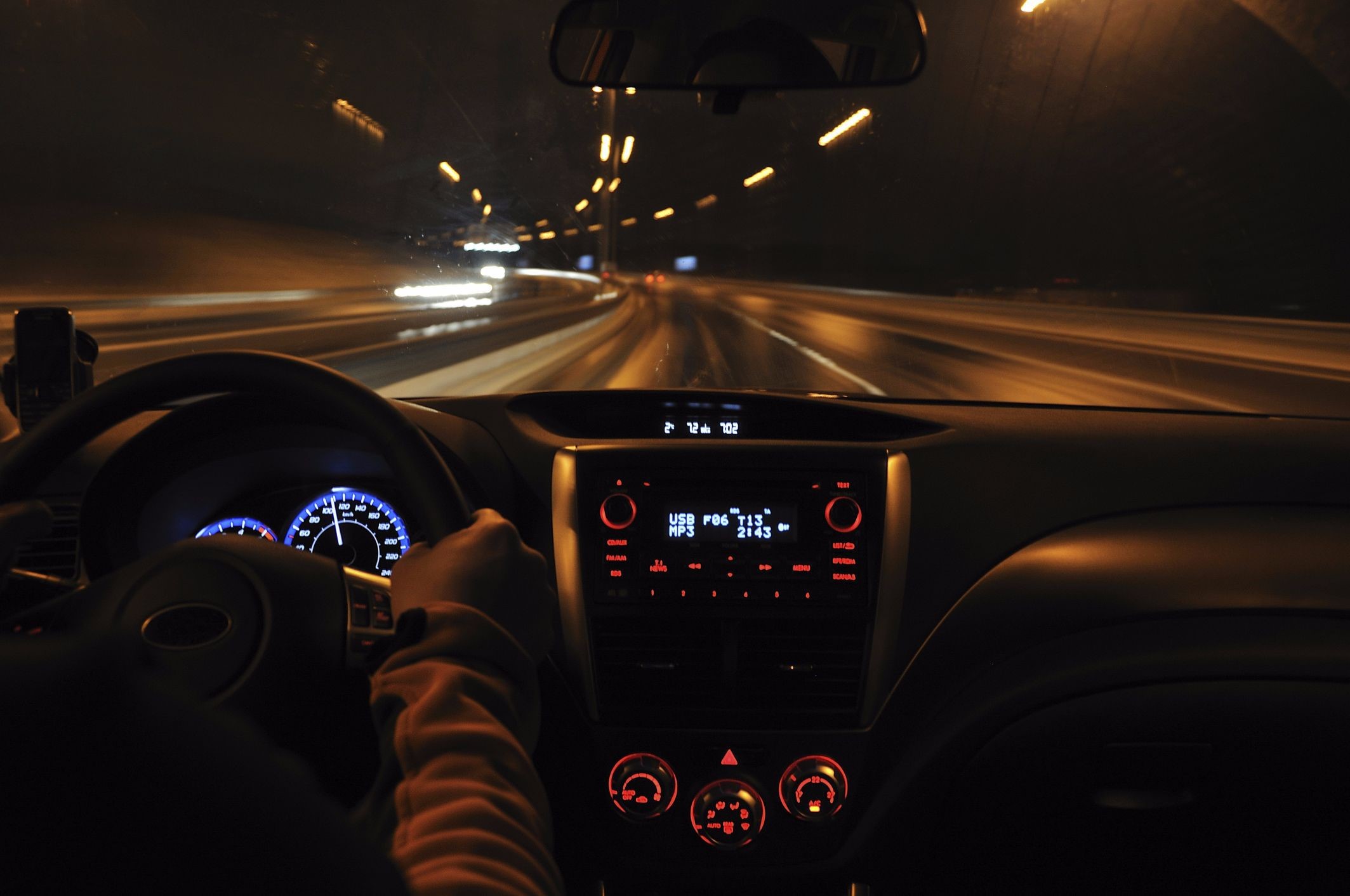 Driver’s-eye view of a car traveling through a tunnel at night, with illuminated dashboard instruments