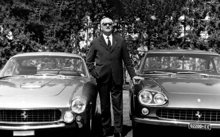 Enzo Ferrari stands between two classic Ferrari cars during a historic outdoor photograph