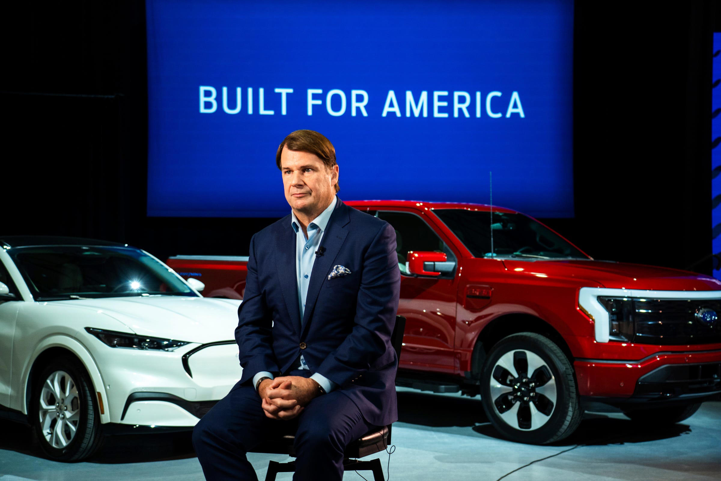 Ford CEO Jim Farley sits between vehicles during a “Built for America” presentation