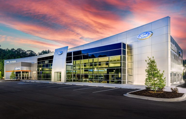 Ford dealership showcasing its modern glass-fronted showroom beneath a colorful sunset sky