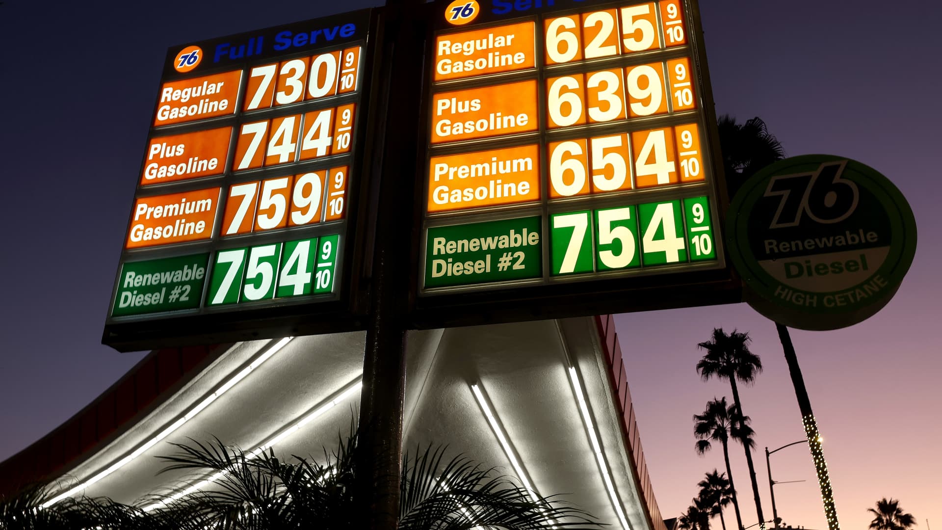 Gas station fuel price signs illuminated at dusk, showing gasoline and diesel prices