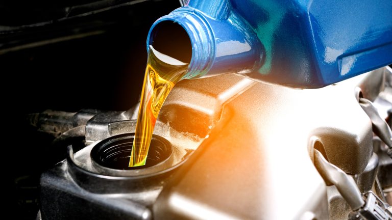 Golden engine oil pours from a blue container into a car’s engine oil filler