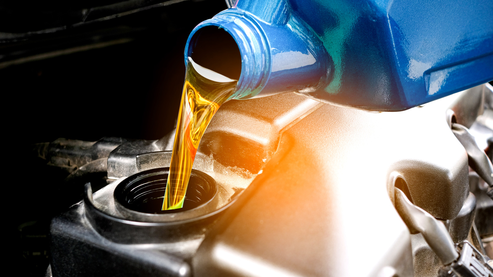 Golden engine oil pours from a blue container into a car’s engine oil filler