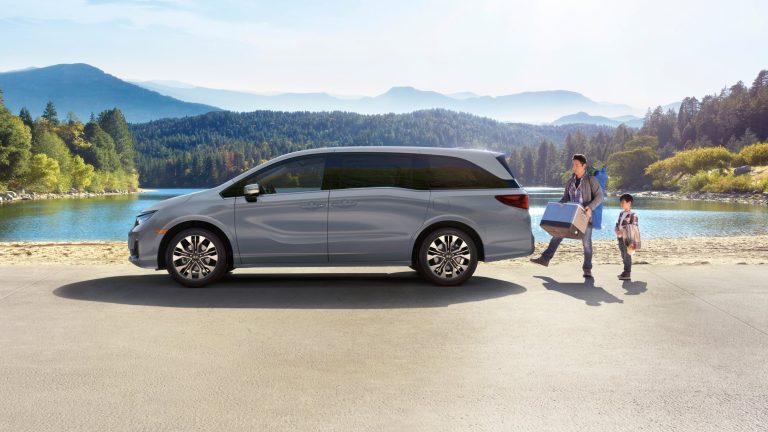 Gray Honda Odyssey parked beside a scenic lake, with a family unloading luggage for an outdoor getaway