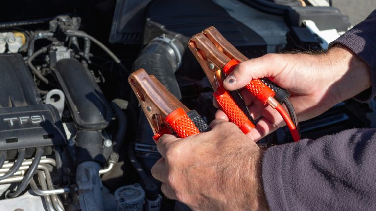 Hands connect jumper cables beneath a car hood during a battery jump-start procedure