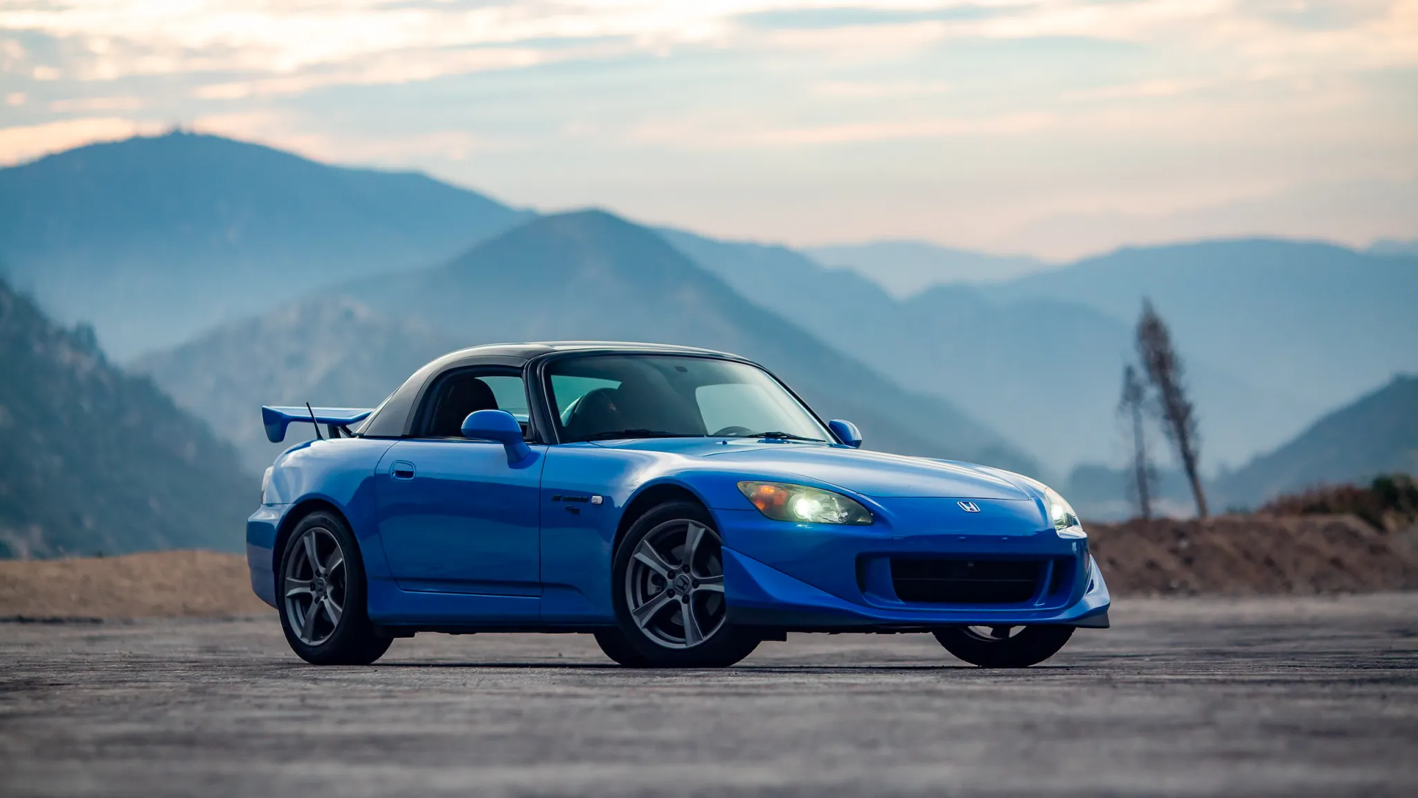 A Honda in blue is standing on an open road with a hilly background