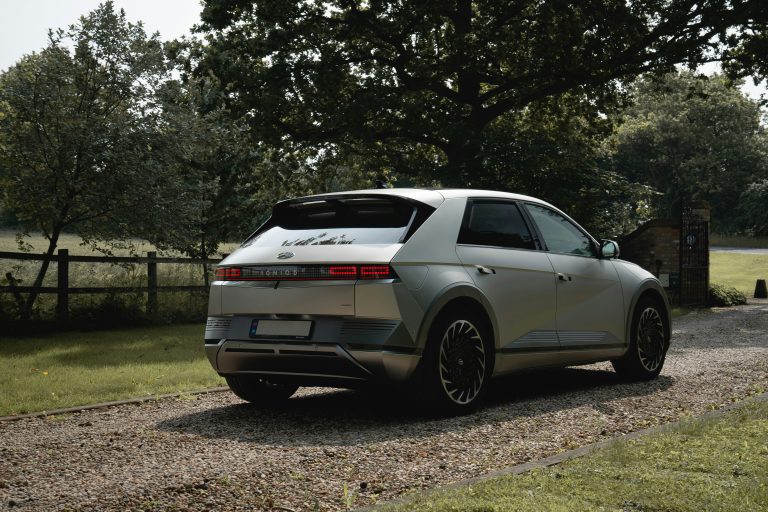 Hyundai Ioniq 5 is stanidng on a grassy road near a tree
