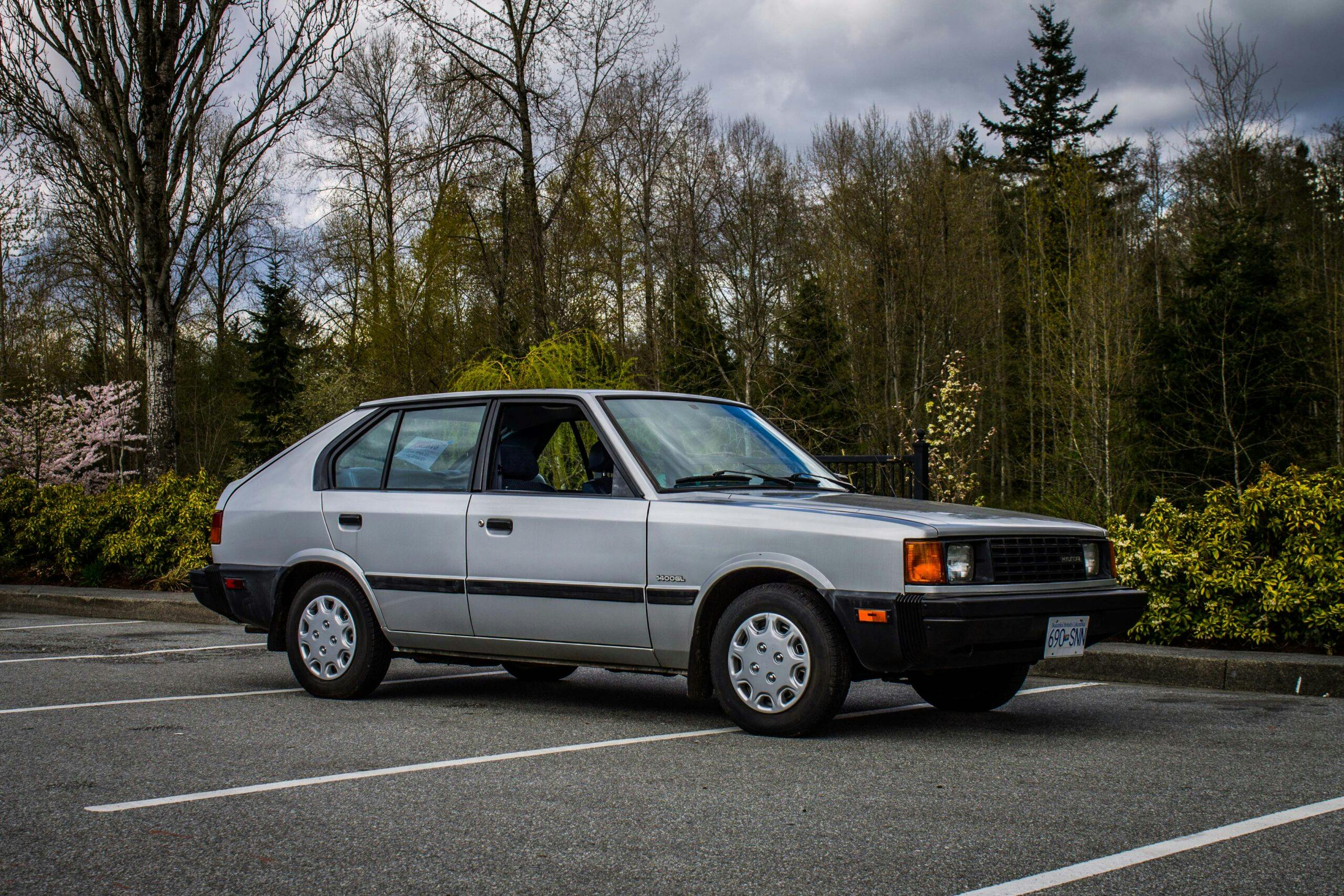 Hyundai Pony parked in a quiet lot surrounded by trees under cloudy skies