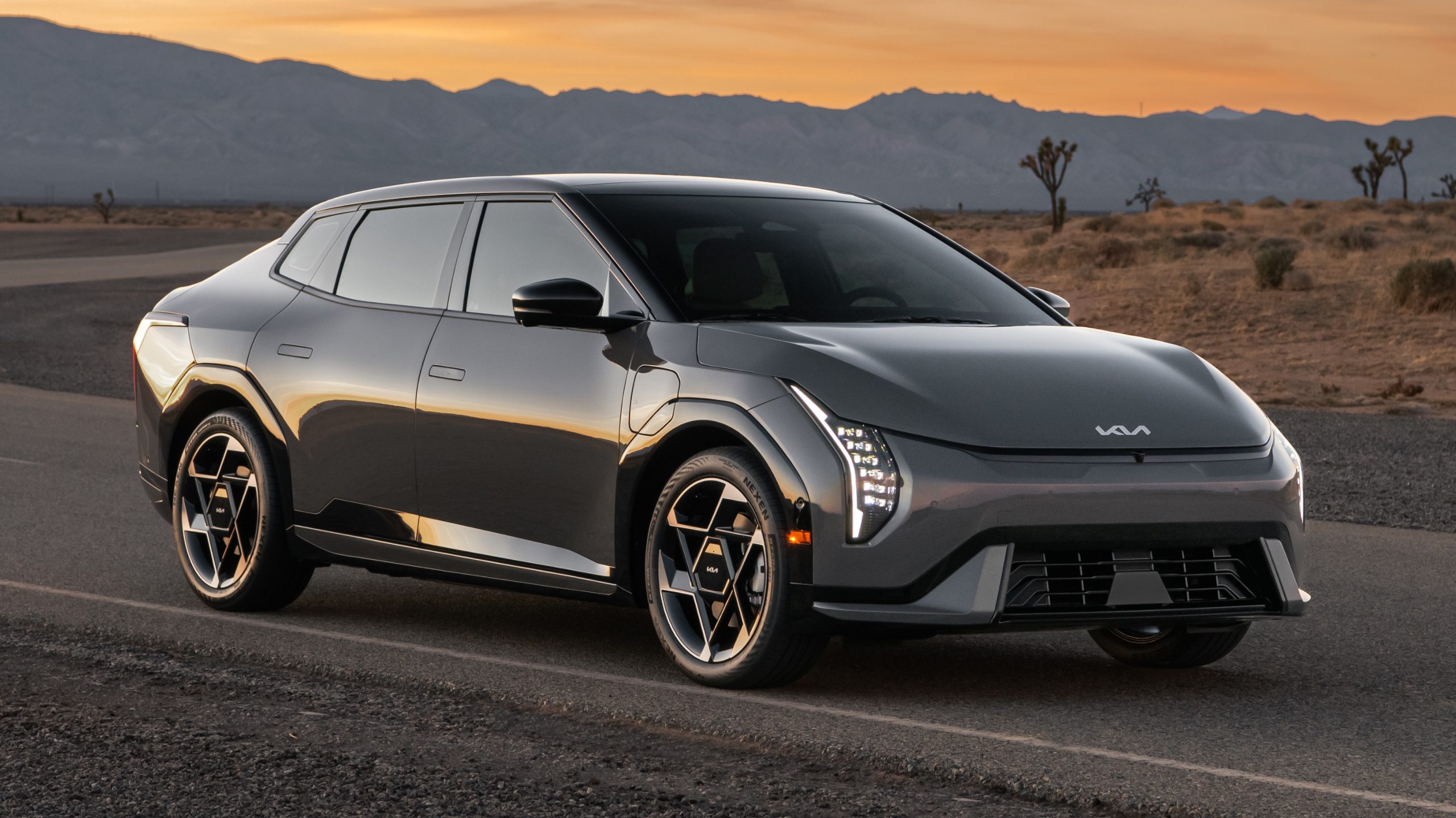 Kia EV4 sedan parked on a desert road with mountains beneath a sunset sky