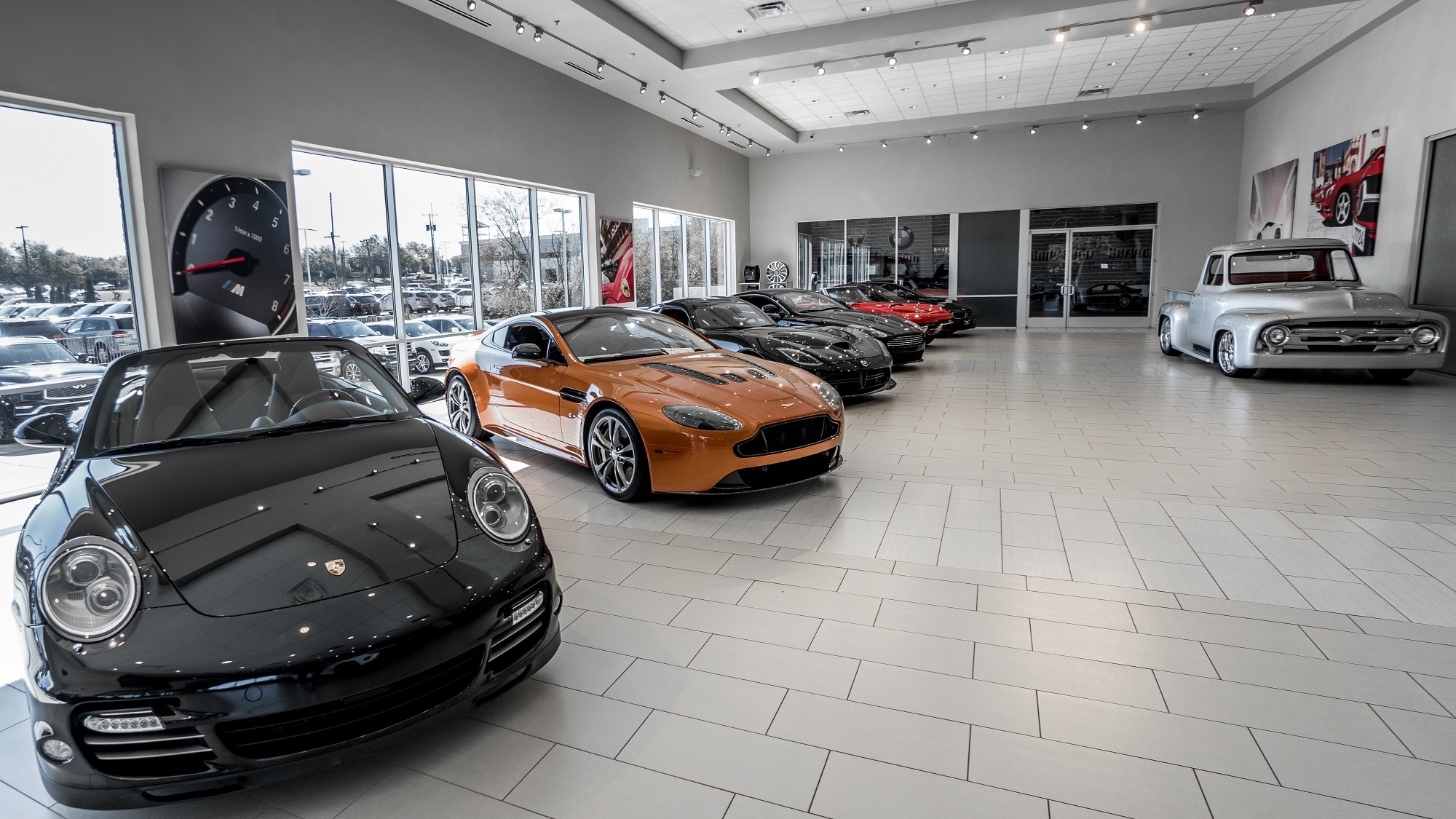 Luxury car dealership showroom displaying premium sports cars, exotic vehicles, and a classic pickup truck