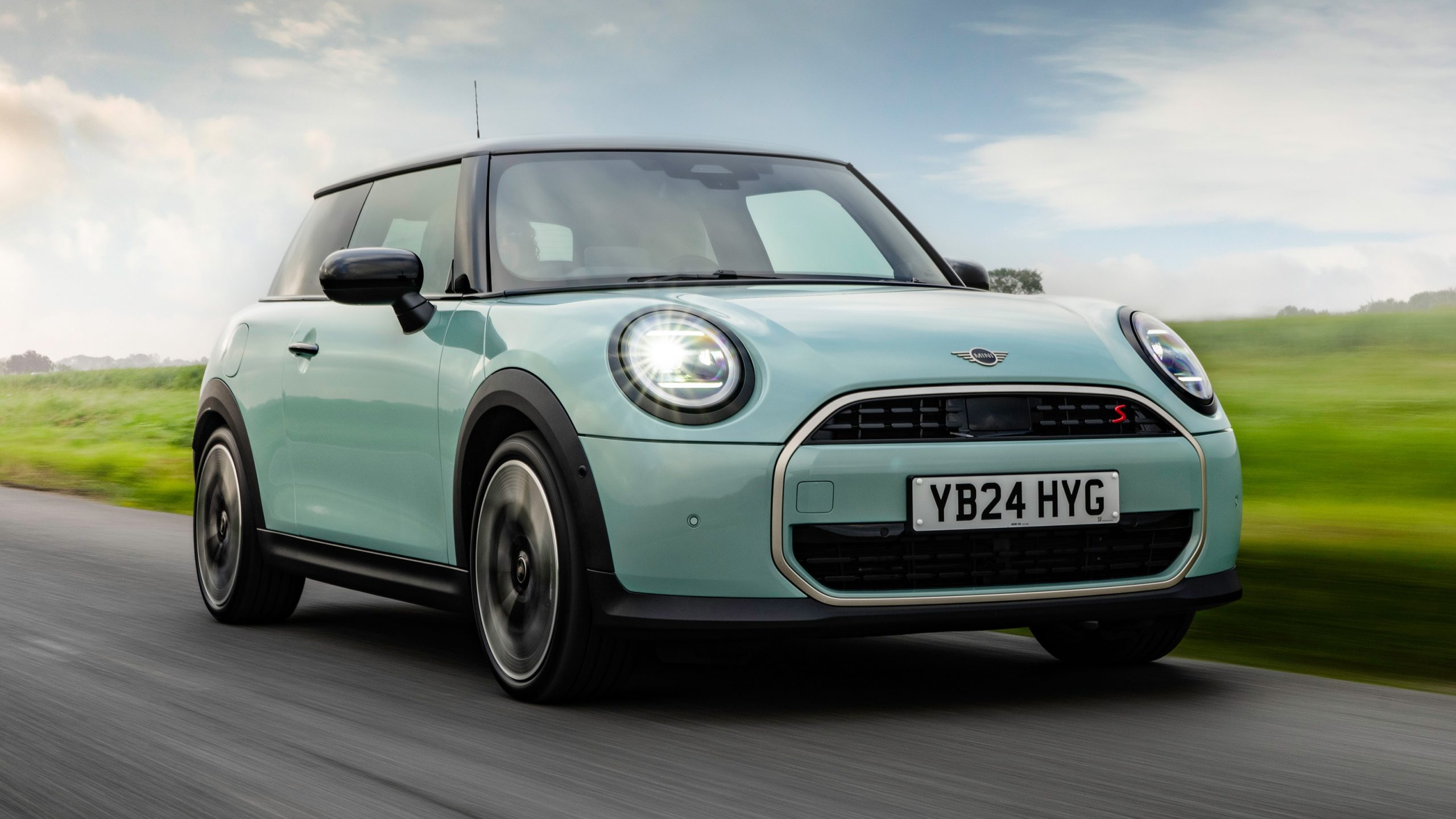 MINI Cooper drives along a scenic countryside road with rolling fields and open skies