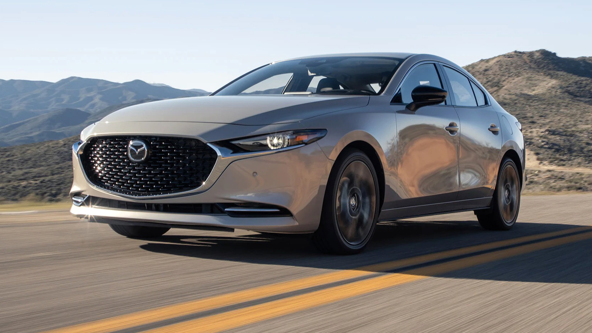 Mazda3 sedan driving along a winding mountain road under clear skies