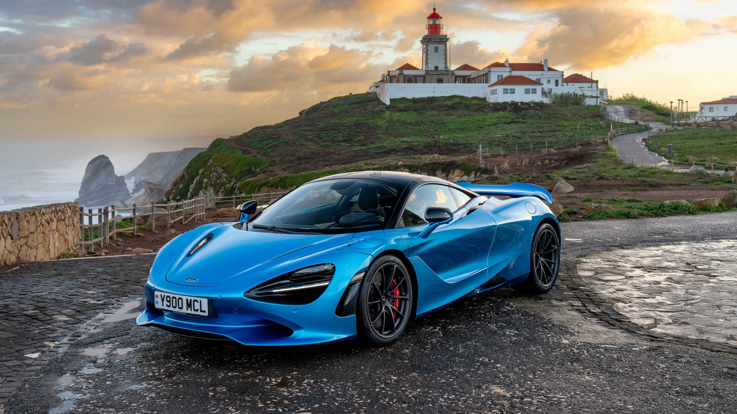 McLaren 750S parked near a coastal lighthouse on a scenic mountain road