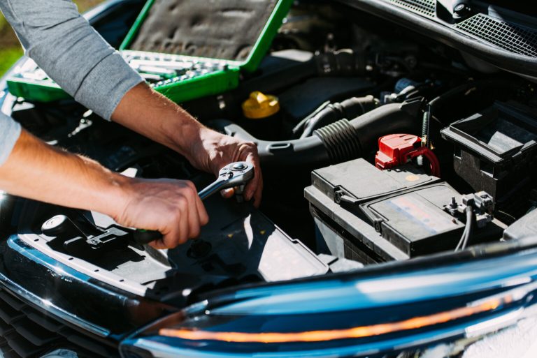Mechanic inspecting a car battery and engine bay with a ratchet wrench during routine vehicle maintenance