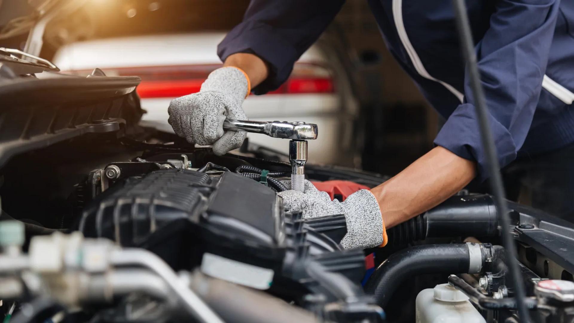 Mechanic wearing protective gloves repairs an engine using a ratchet wrench during routine vehicle maintenance