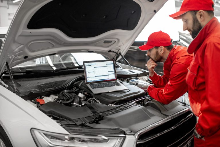 Mechanics perform engine diagnostics using a laptop during an inspection inside a professional auto repair workshop