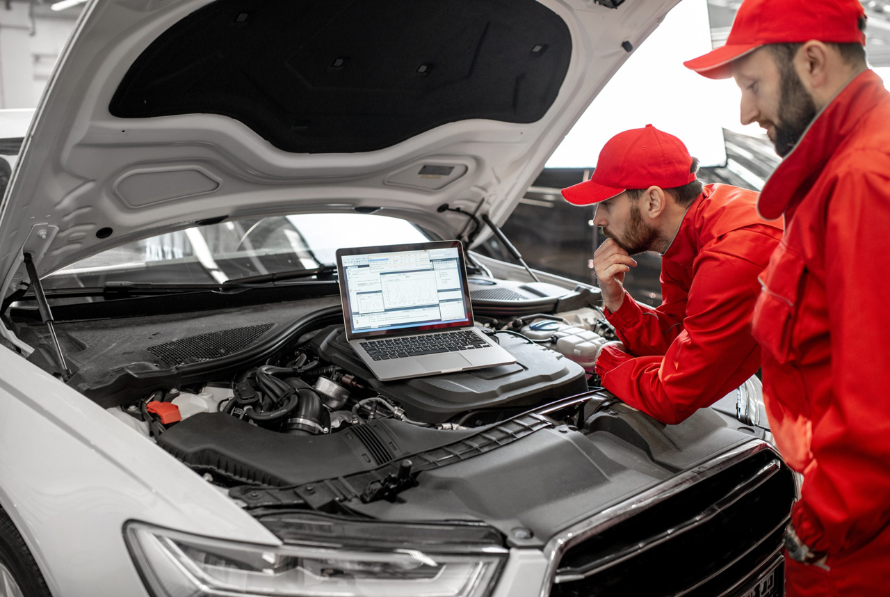 Mechanics perform engine diagnostics using a laptop during an inspection inside a professional auto repair workshop