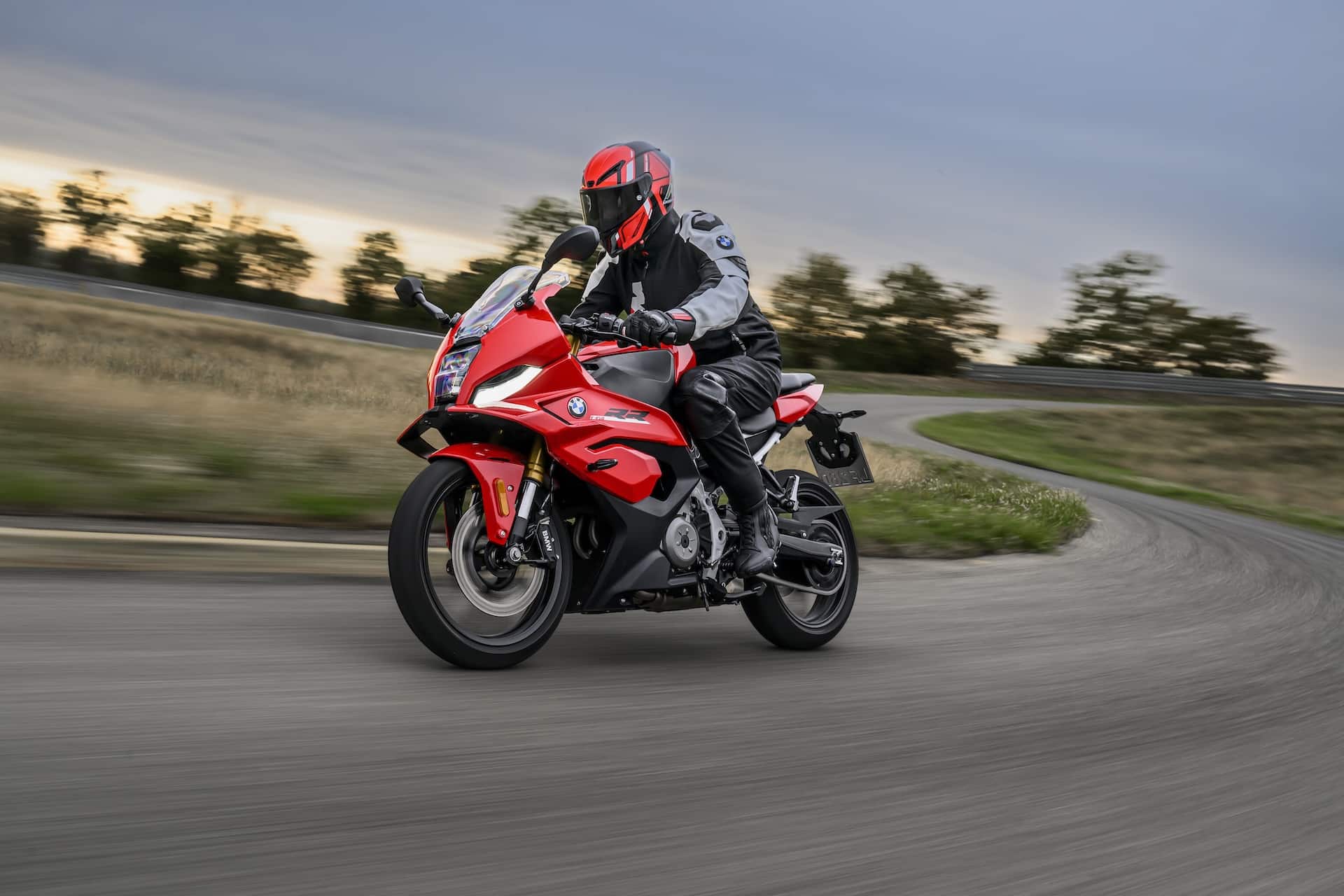 Motorcyclist riding a red BMW adventure bike through a winding country road at sunset