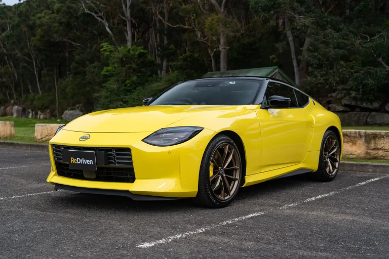 A yellow Nissan Z is standing in a backyard parking on a sunny day