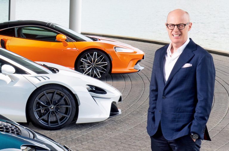 Porsche CEO Michael Leiters stands beside McLaren supercars during an automotive event